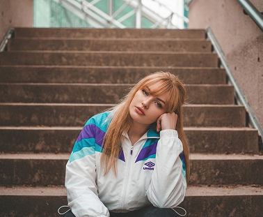 Chica rubia en unas escaleras posando con una chaqueta Umbro